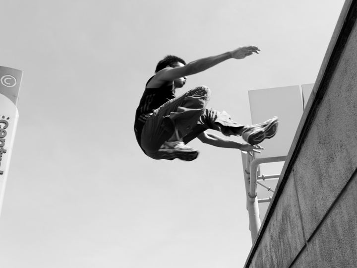 Black and white photo of a parkour athlete in flight beside a tall wall