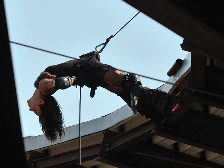 A stuntwoman hanging in a harness high above a stunt show arena