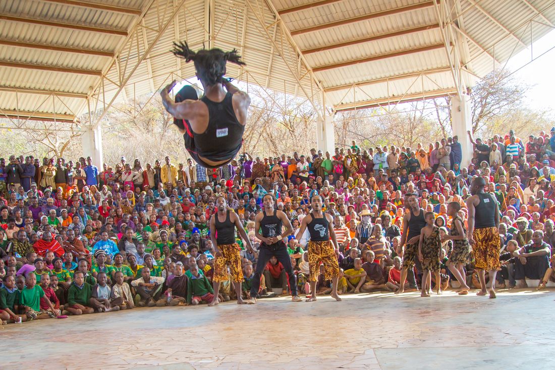 An acrobat flipping above a large seated crowd under a canopy